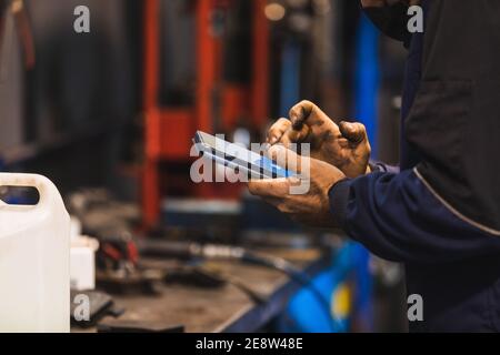 Mechanic using cell phone in the workshop. Hands full of grease. Technology concept. Stock Photo