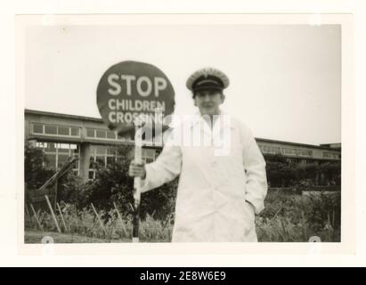 Soft focus - early 1960's photograph of a lollipop lady on patrol at a school crossing, outside a school, holding a Stop children crossing sign, Lincoln, England, U.K. Stock Photo