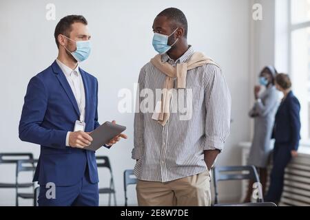 Waist up portrait of two businessmen wearing masks and chatting during break at business conference, copy space Stock Photo