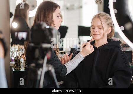 Woman making a video for her blog of making makeup, digital camera on tripod. Young female blogger on camera screen while doing makeup Stock Photo