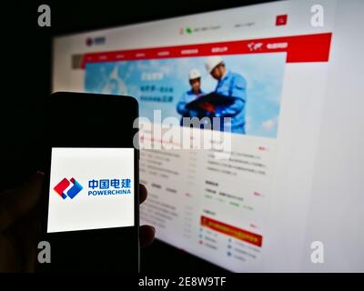 Person holding phone with logo of engineering company Power Construction Corporation of China (POWERCHINA) with website. Focus on smartphone screen. Stock Photo