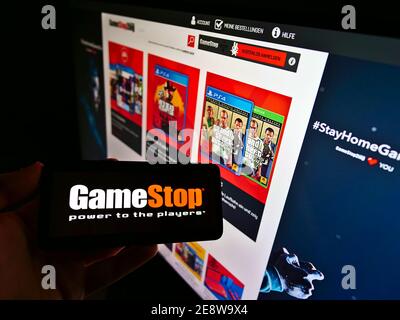 Holding cellphone with business logo of US retail company GameStop Corp. in front of website with online shop. Focus on mobile phone screen. Stock Photo