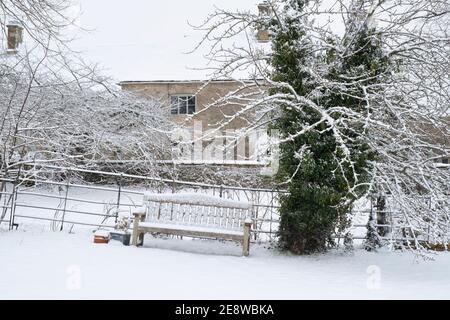 Wooden bench in St Marys churchyard in the snow. Swinbrook, Cotswolds, Oxfordshire, England Stock Photo