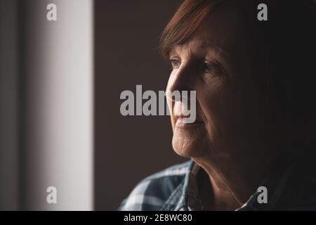 Close-up portrait of senior woman with dementia who is looking through window. Stock Photo