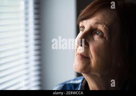 Close-up portrait of senior woman with dementia who is looking through window. Stock Photo