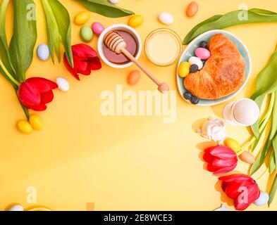Spring breakfast with croissants and berries. Easter chocolate eggs, red tulips on a yellow background. Copy space. Flat lay Stock Photo
