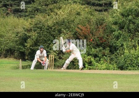 Wicket keeper and cricket batsman about to hit the cricket ball, during a local village cricket match. England UK