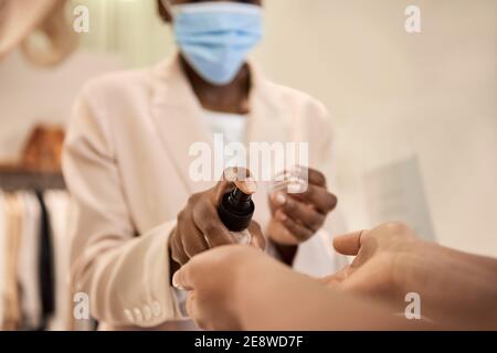 African American boutique owner spraying sanitizer on a customer's hands Stock Photo