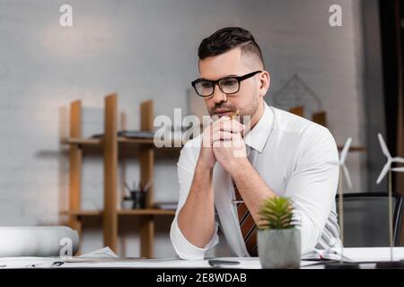 thoughtful architect sitting at workplace near models of wind turbines on blurred foreground Stock Photo
