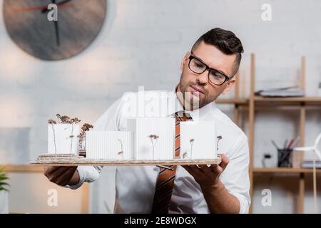 serious architect holding houses models in architectural bureau Stock Photo