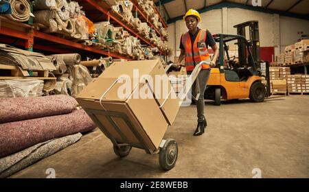 African female warehouse worker moving boxes with a dolly Stock Photo