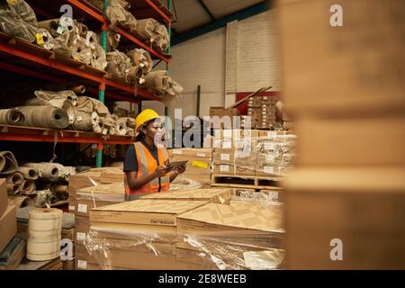 African female warehouse worker checking boxes using a digital tablet Stock Photo