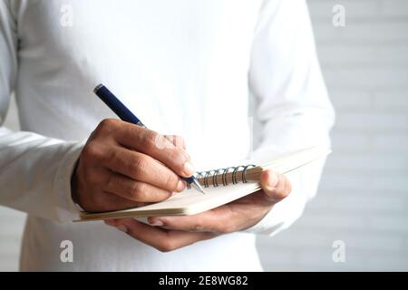 Close up of man in casual white shirt writing on notepad. Stock Photo