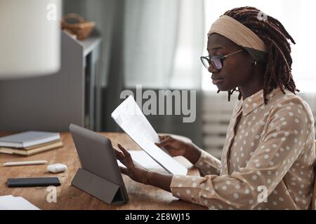 Side view portrait of young African-American woman wearing glasses and using digital tablet on stand while working from home, copy space Stock Photo