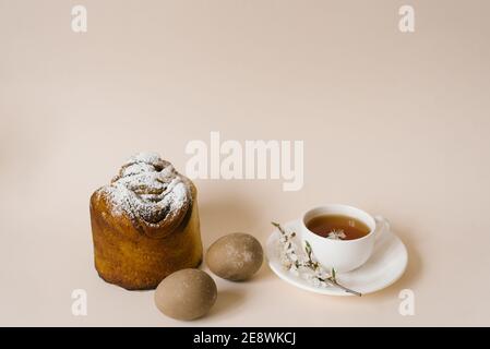 An Easter composition with a cake and eggs and a cup of tea with a sprig of a flowering apple tree on a light background. Easter vacation breakfast co Stock Photo