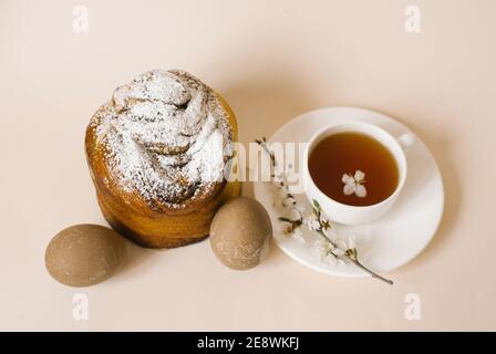 A traditional Easter cake sprinkled with powdered sugar, colored beige eggs and a cup of black tea in a white mug and a sprig of apple blossom. Holida Stock Photo