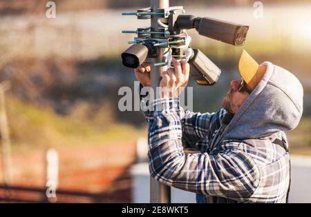 Caucasian CCTV Technician in His 40s Installing IP Cameras on a Pole During Cold Weather. Modern Digital Network Security Cameras. Surveillance and Se Stock Photo