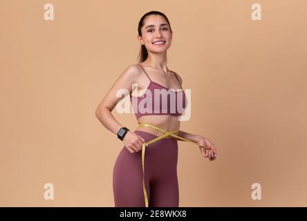 Smiling Young Woman Measuring Waist And Looking At Camera Stock Photo