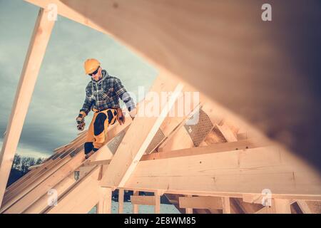Caucasian Wooden House Skeleton Frame Construction Worker in His 40s on the Newly Built Roof Frame. New Home Development Theme.