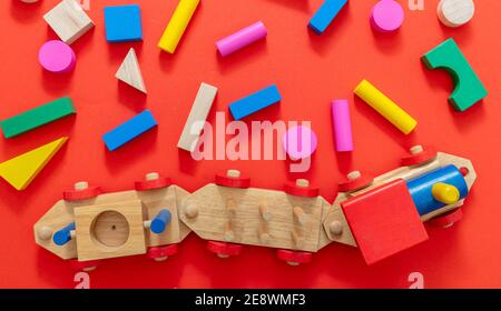 Train children toy and blocks, creative preschool kids play. Wooden colorful blocks construction on red color background, top view. Stock Photo