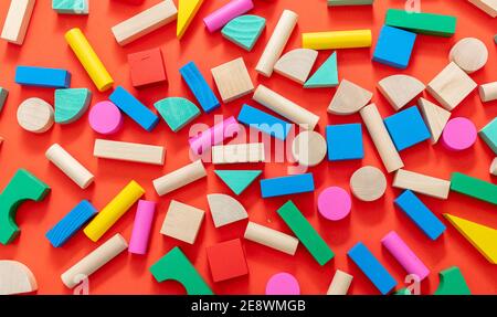 Wood toy block pieces and shapes background. Children, creative preschool kids play. Wooden colorful cubes on red color background, top view. Stock Photo