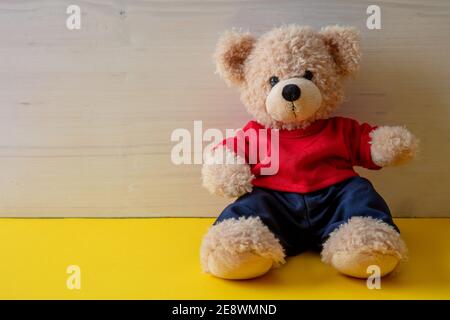 Teddy bear sitting in an empty room, yellow color floor, white wood wall background, Kid alone wearing red tshirt in the child room Stock Photo