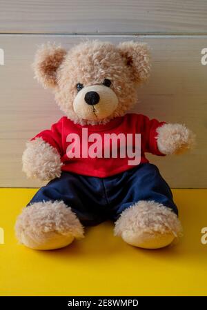 Teddy bear sitting in an empty room, yellow color floor, white wood wall background, Kid alone wearing red tshirt in the child room Stock Photo