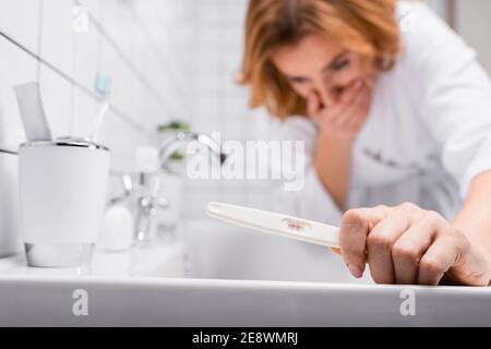 pregnancy test in hand on pregnant woman in bathrobe feeling nausea on blurred background Stock Photo