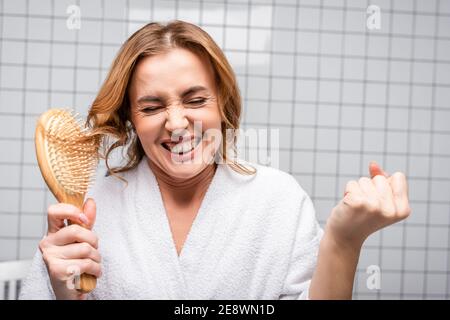 amazed woman in white bathrobe brushing hair in bathroom Stock Photo