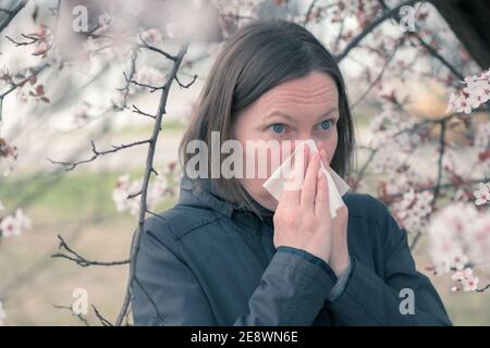 Woman sneezing in front of blooming cherry tree in spring allergy concept, selective focus