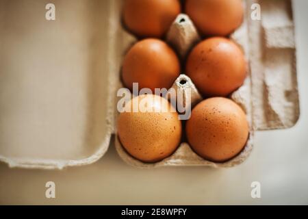 A cardboard box of brown chicken eggs from the store sits on the kitchen table, illuminated by the light. Food for breakfast. Stock Photo