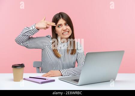 Depressed overworked business woman holding fingers near temple imitating gun shot, feeling stress and pressure because of work problems. Indoor studi Stock Photo