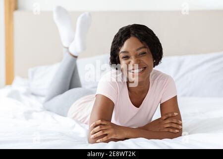 Positive black lady in pajamas laying on bed Stock Photo