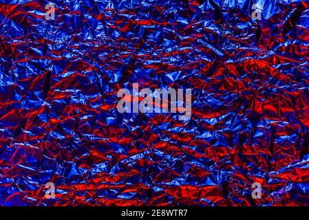 Red and blue foil background with shiny crumpled surface for texture background. Iridescent surface wrinkled foil. Stock Photo