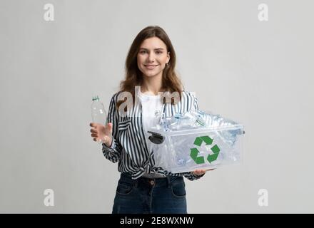 Plastic Recycle. Smiling Young Woman Collecting Bottles For Waste Recycling To Container Stock Photo