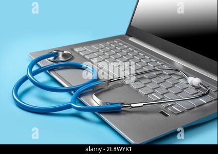 Stethoscope On Laptop Keyboard on blue background. Modern medical technology and sofware advances concept. Doctor's working table with stethoscope aco Stock Photo