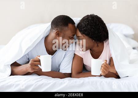 Romantic black couple laying under blanket, drinking tea Stock Photo