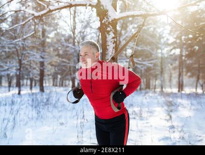 Functional training. Portrait of senior man doing exercises with TRX fitness straps at snowy park in winter Stock Photo