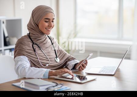 Cheerful muslim woman doctor using digital tablet and smartphone Stock Photo