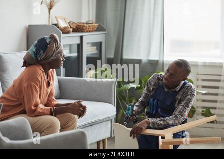 Side view portrait of African-American handyman helping young woman repair or assemble furniture, copy space Stock Photo