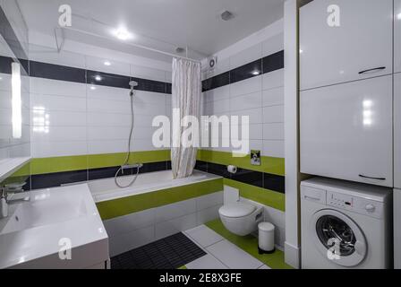 Contemporary interior of bathroom in modern flat. Black and green tile. Bath with shower. Toilet. Washing machine. Stock Photo