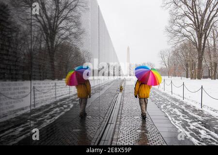 A man carrying colorful umbrella visits the Vietnam Veterans Memorial during a snowy day in Washington, D.C. The Washington Monument can be seen in th Stock Photo