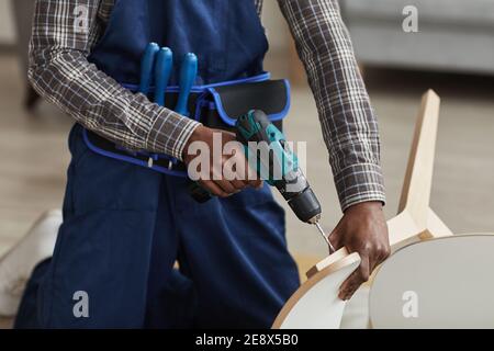 Cropped portrait of unrecognizable African-American handyman holding electric screwdriver while assembling furniture in home interior, copy space Stock Photo