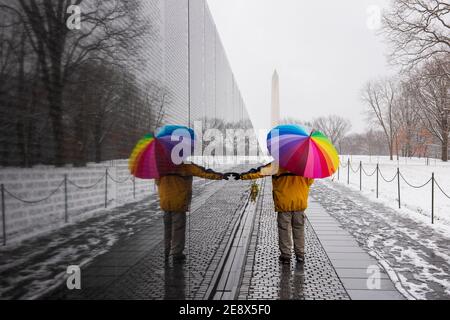 A man carrying colorful umbrella visits the Vietnam Veterans Memorial during a snowy day in Washington, D.C. The Washington Monument can be seen in th Stock Photo