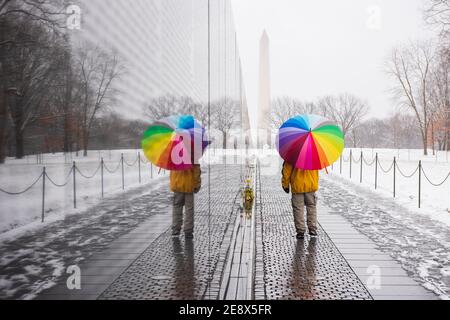 A man carrying colorful umbrella visits the Vietnam Veterans Memorial during a snowy day in Washington, D.C. The Washington Monument can be seen in th Stock Photo