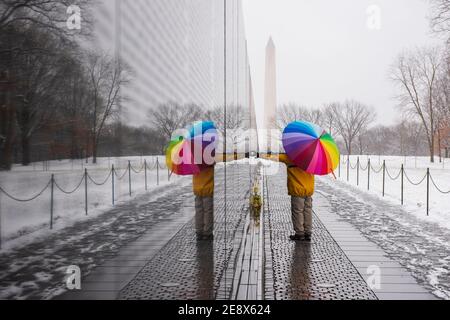 A man carrying colorful umbrella visits the Vietnam Veterans Memorial during a snowy day in Washington, D.C. The Washington Monument can be seen in th Stock Photo