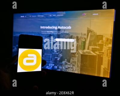 Person holding smartphone with logo of British taxi software development company Autocab Ltd on display in front of website. Focus on phone screen. Stock Photo
