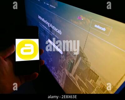 Person holding cellphone with logo of British taxi software development company Autocab Ltd on display in front of web page. Focus on phone screen. Stock Photo