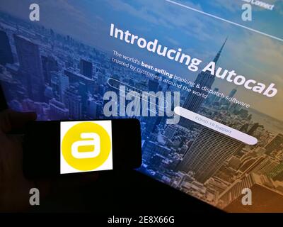 High angle view of person holding mobile phone with logo of British taxi software development company Autocab Ltd on display. Focus on phone screen. Stock Photo