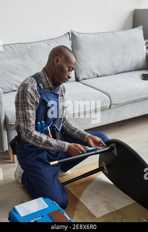 Vertical side view portrait of African-American handyman assembling furniture in home interior, service and assistance concept Stock Photo
